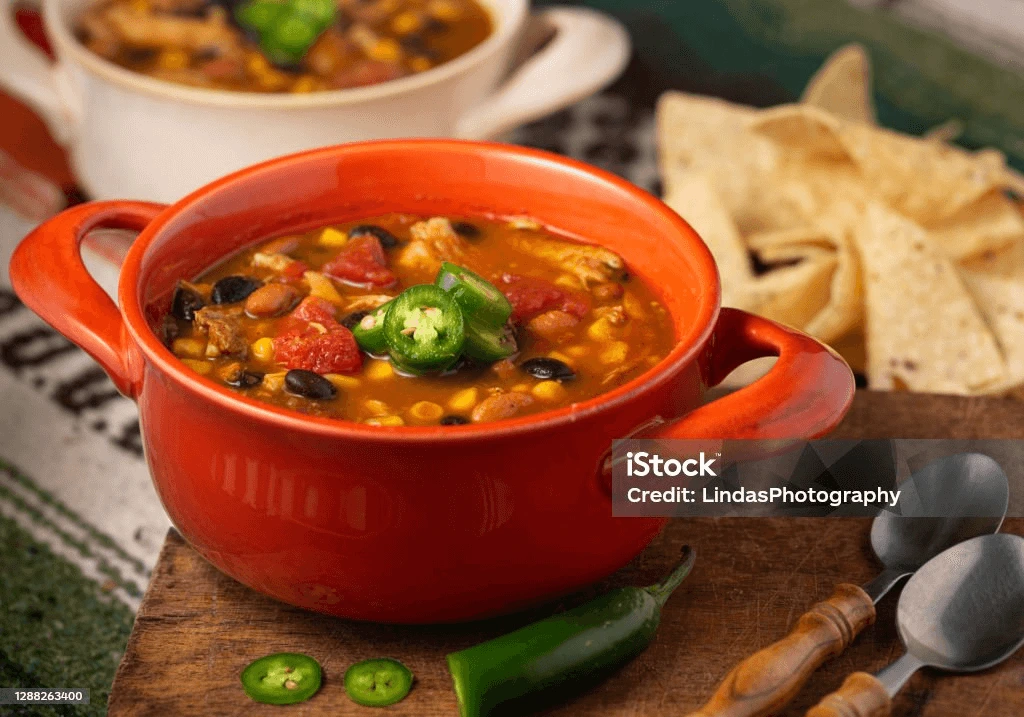 Close-up of a hearty bowl of taco soup topped with sour cream, shredded cheese, tortilla chips, and fresh cilantro.
